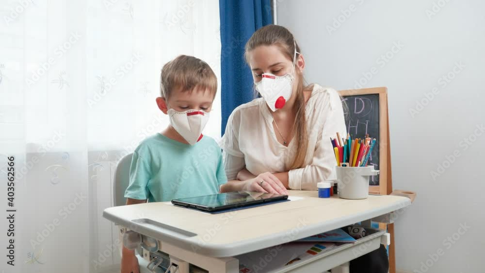 Mother with little son wearing protective medical respirator masks using tablet computer. Doing homework and studying at home during lockdown and self isolation. Remote school concept Mother with little son wearing protective medical respirator masks using tablet computer. Doing homework and studying at home during lockdown and self isolation. Remote school concept