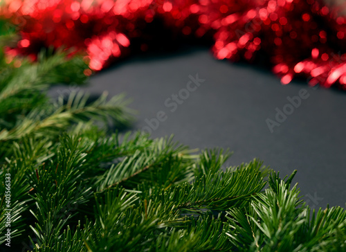 Black background with fir branches on the left corner and red tinsel to decorate the Christmas tree on the right.