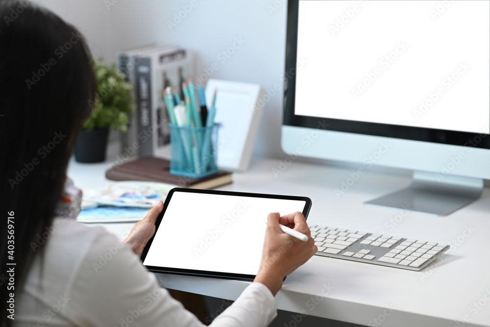 Rear view of female graphic designer working on digital tablet at her creative workspace. Rear view of female graphic designer working on digital tablet at her creative workspace.