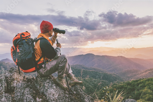 Hikers with backpacks holding binoculars sitting on top of the rock mountain