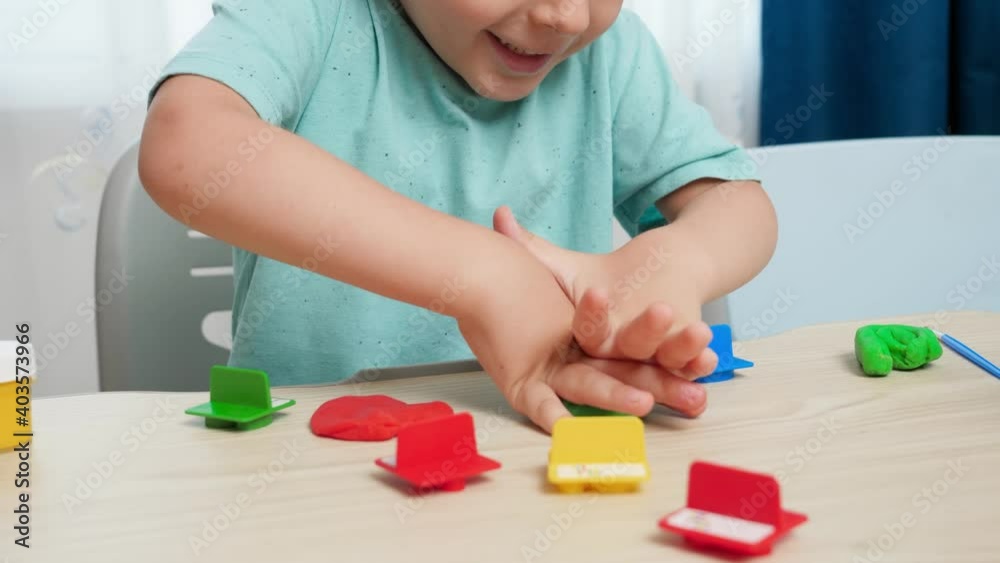 Closeup video of little boy using plastic forms for shaping and sculpting toy plasticine or dough. Child hobby on school desk at home