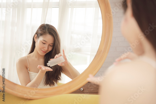 Asian beauty woman using facial lotion cream infront of the mirror.