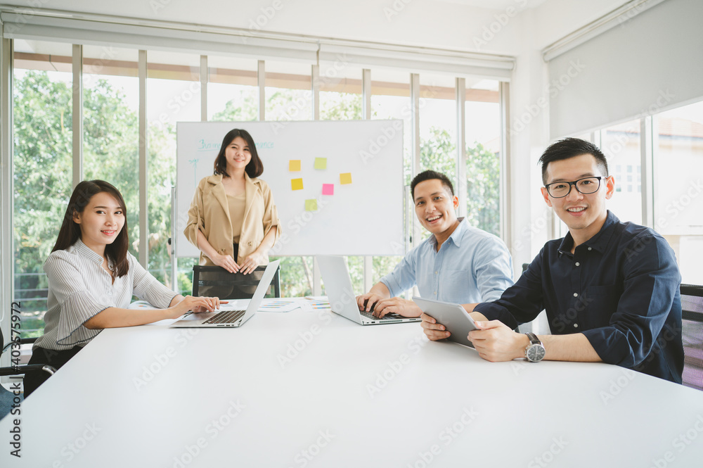 Fototapeta premium Happy group of young Asian business people during brainstorm meeting conference for new project. Man looking at camera and smiling.