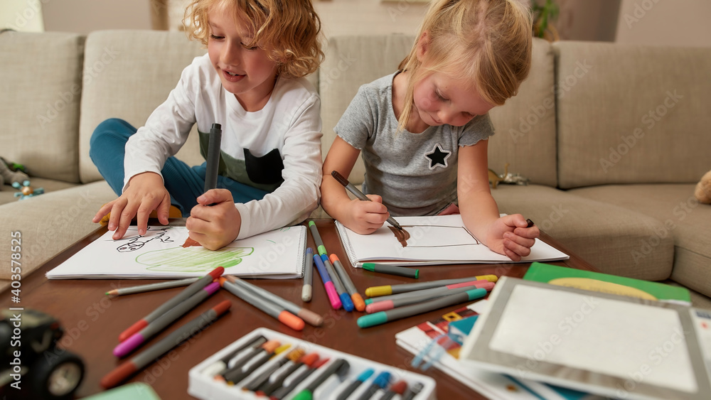 Cute little boy and girl painting with markers in living room while spending time together at home Cute little boy and girl painting with markers in living room while spending time together at home