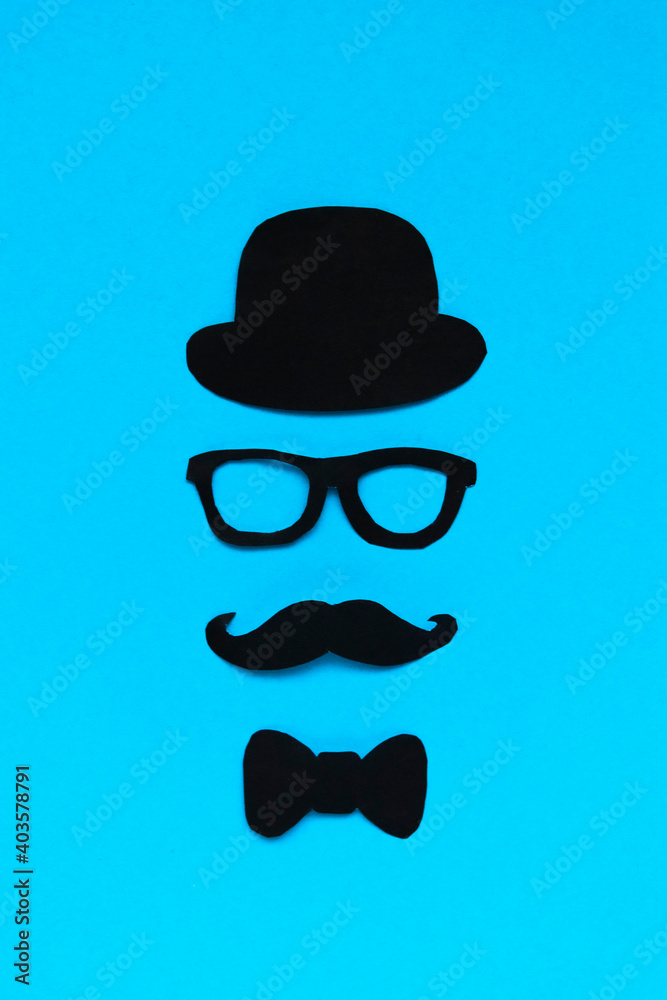 Happy Father's Day concept. Composition of paper decor hat, glasses, bow tie and mustache on blue background