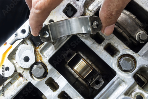 Bild auf Leinwand The hand of an auto mechanic picks up the engine connecting rod bearing in check with the engine's crankshaft on background