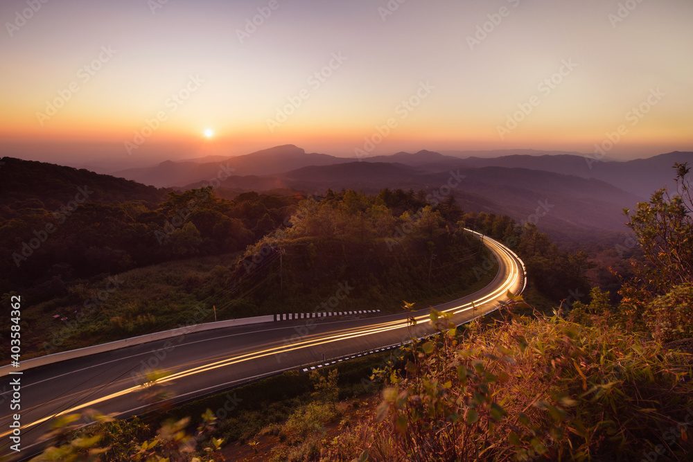 Light trails at beautiful sunset, long exposure image. Straight single lane asphalt road stretching into the distance with mountains in the background. Holiday.