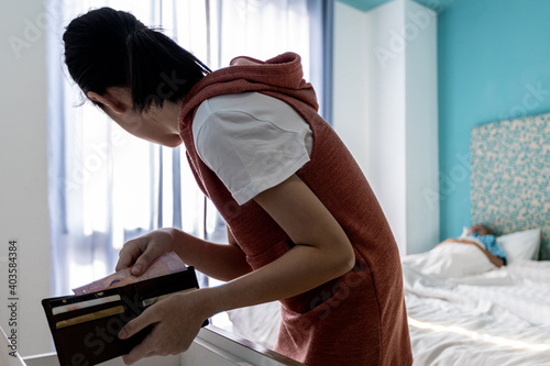 Fototapeta Careful Teenager girl opens a wallet and pulls cash with her hand from the purse,asian woman is quietly trying to steal her parents money in a bedroom at home,bad behavior,concept of theft,burglary