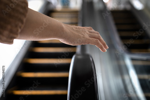 Avoid and Don't touch with objects that are frequently touched for safety,hand of girl was about to touch the handrail of escalator at risk of Coronavirus infection,contaminated with germs or COVID-19