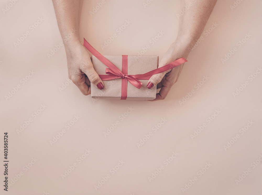Woman hands holding gift decorated with red ribbon on pink background, copy space. Flat lay, hands and present box, top view. Valentine or love, spring holidays, Christmas and birthday concept.