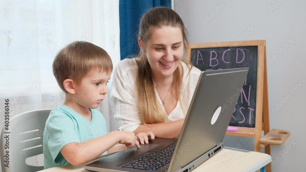 Smiling mother teaching her little son using laptop computer during education and studying at home. Concept of remote school and distance education at home Smiling mother teaching her little son using laptop computer during education and studying at home. Concept of remote school and distance education at home