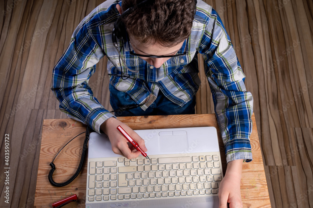Boy with shirt and glasses makes notes on laptop with fountain pen Boy with shirt and glasses makes notes on laptop with fountain pen