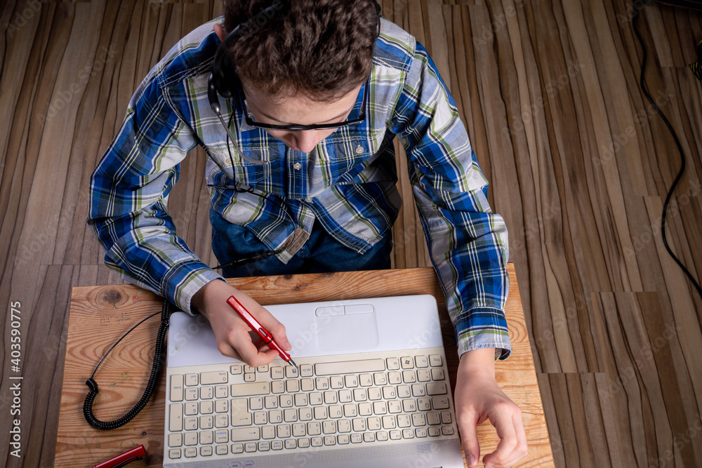 Boy with shirt and glasses makes notes on laptop with fountain pen Boy with shirt and glasses makes notes on laptop with fountain pen
