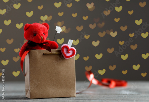 Creative holiday image of teddy bear sitting in a shopping bag. Gift box, heart symbol and fairy-lights on a background. Valentine's day concept
