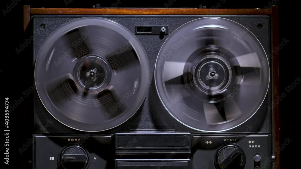 Male hands include rewind on vintage reel to reel tape recorder against a black studio background. Retro music player. Front view close up. Popular disco trends 70s, 80s. Slow motion.