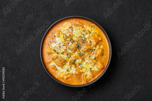 Murgh Makhani or Butter Chicken in black bowl on dark slate table top. Indian Cuisine dish with chicken meat and creamy masala. Asian food and meal. Top view