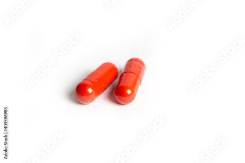 Three Red Pills Capsules with Many in Background Isolated on a White
