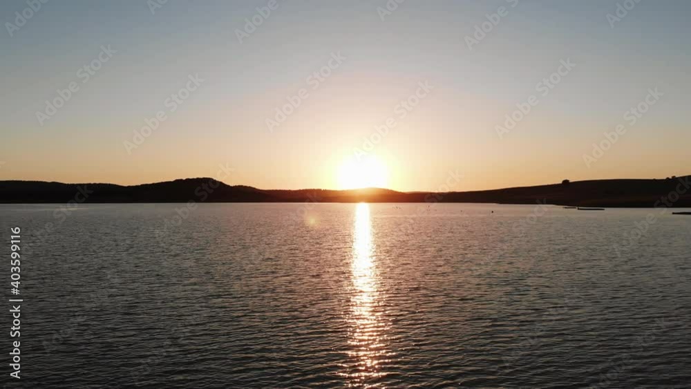 Golden sunset almost hiding behind the mountains on the horizon, lighting Wakana lake in Cádiz, Spain - Aerial Fly-over tilt up reveal Golden sunset almost hiding behind the mountains on the horizon, lighting Wakana lake in Cádiz, Spain - Aerial Fly-over tilt up reveal