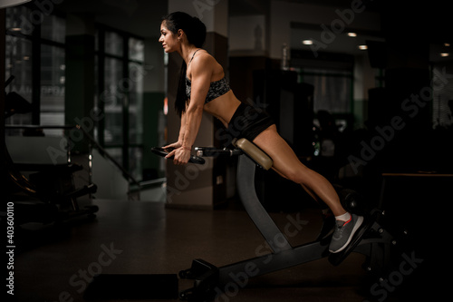 Side view of attractive muscular woman working out on simulator in the gym.