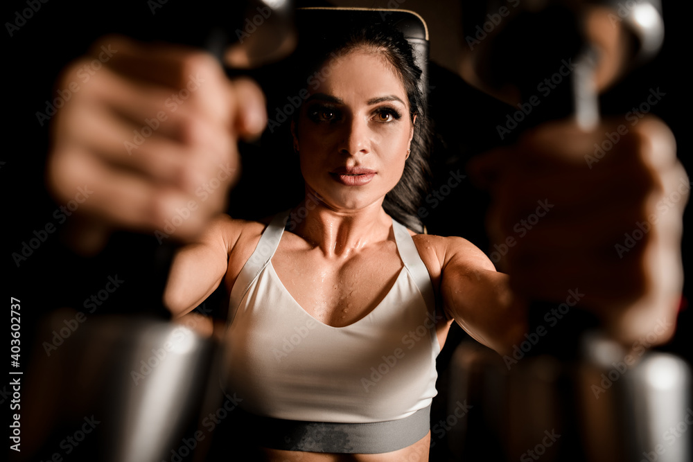 Close-up of woman who using machine for pumping group of muscles in gym.
