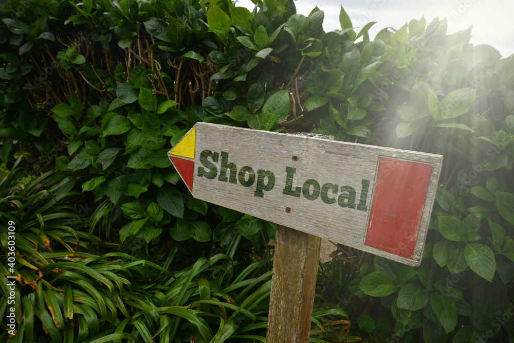 vintage old wooden signboard with text shop local near the green plants.