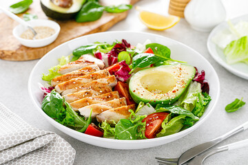 Grilled chicken meat and fresh vegetable salad of tomato, avocado, lettuce and spinach. Healthy and detox food concept. Ketogenic diet. Buddha bowl dish on white background