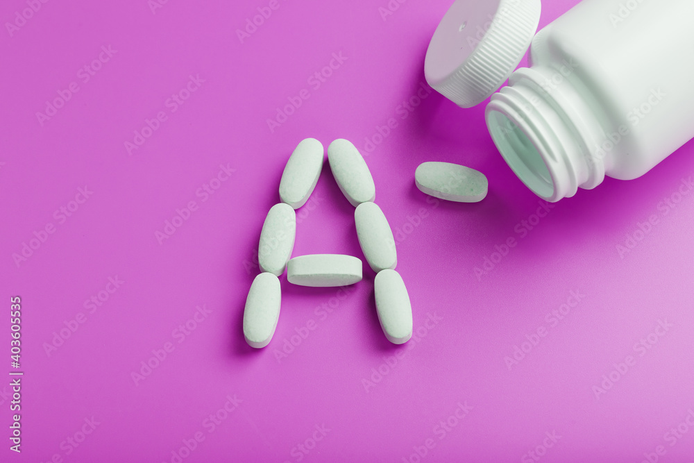 Vitamin A pills fell out of a white jar on a pink background.