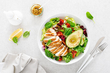 Grilled chicken meat and fresh vegetable salad of tomato, avocado, lettuce and spinach. Healthy and detox food concept. Ketogenic diet. Buddha bowl dish on white background, top view