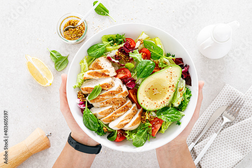 Grilled chicken meat and fresh vegetable salad of tomato, avocado, lettuce and spinach. Healthy and detox food concept. Ketogenic diet. Buddha bowl in hands on white background, top view photo