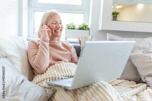 Happy cheerful young woman talking on the phone at home, smiling teen girl making answering call by cellphone sitting on sofa, beautiful lady having pleasant funny conversation speaking by mobile