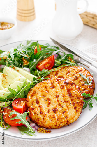 Grilled chicken burgers, avocado and fresh vegetable salad with tomato and arugula