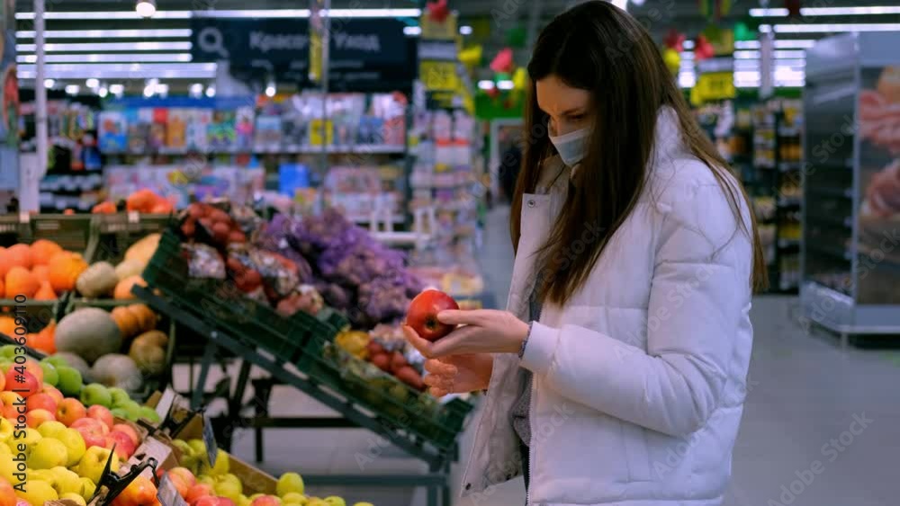 Young brunette woman in a medical mask chooses apples shop. Buying food at the supermarket during the coronavirus and lockdown epidemic Young brunette woman in a medical mask chooses apples shop. Buying food at the supermarket during the coronavirus and lockdown epidemic