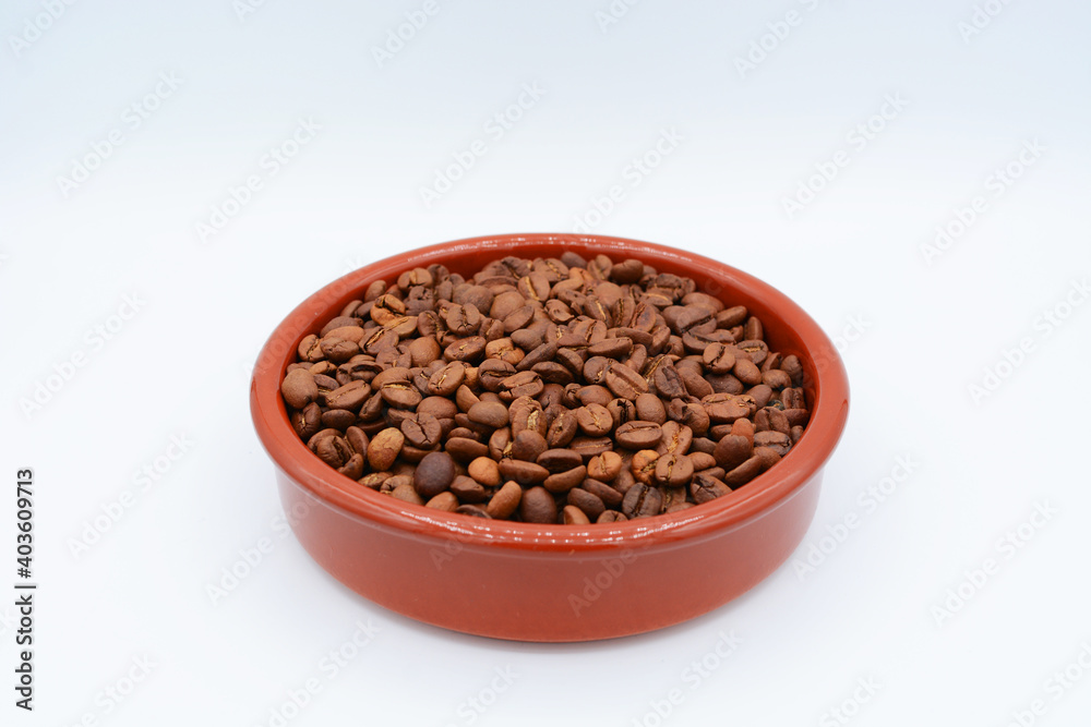 Roasted coffee beans in a round-shaped, brown plate on white background Roasted coffee beans in a round-shaped, brown plate on white background