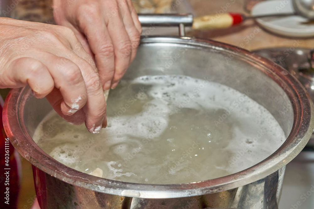 Hands put raw dumplings in boiling water