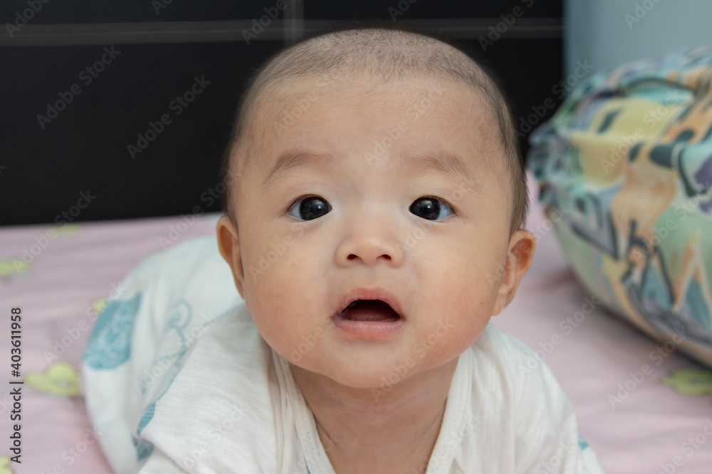 Closeup Portrait Adorable and happy Chinese baby boy on tummy time on bed. Newborn child relaxing in bed
