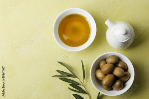 Composition of olive oil, a branch and green olives on a bright background.