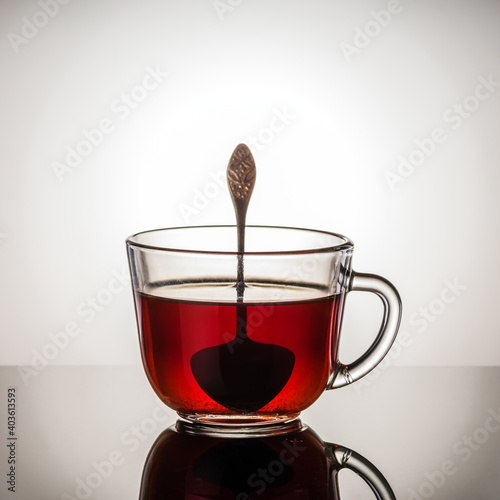 Black tea in a glass cup with a handle and a teaspoon. Photo taken in studio