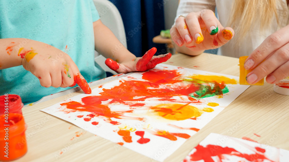 Closeup of adult and child drawing with hands and fingers using colorful paint on white paper. Concept of creative education and art skills development Closeup of adult and child drawing with hands and fingers using colorful paint on white paper. Concept of creative education and art skills development
