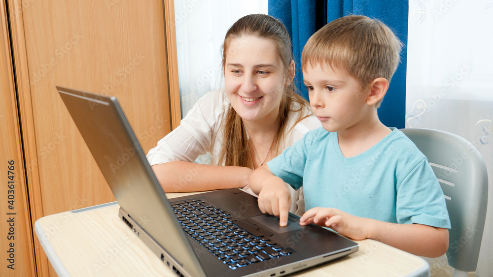 Portrait of young mother with little son working and using laptop computer. Family education at home using computer