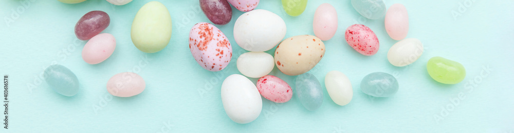 Happy Easter concept. Preparation for holiday. Easter candy chocolate eggs and jellybean sweets isolated on trendy pastel blue background. Simple minimalism flat lay top view copy space. Banner