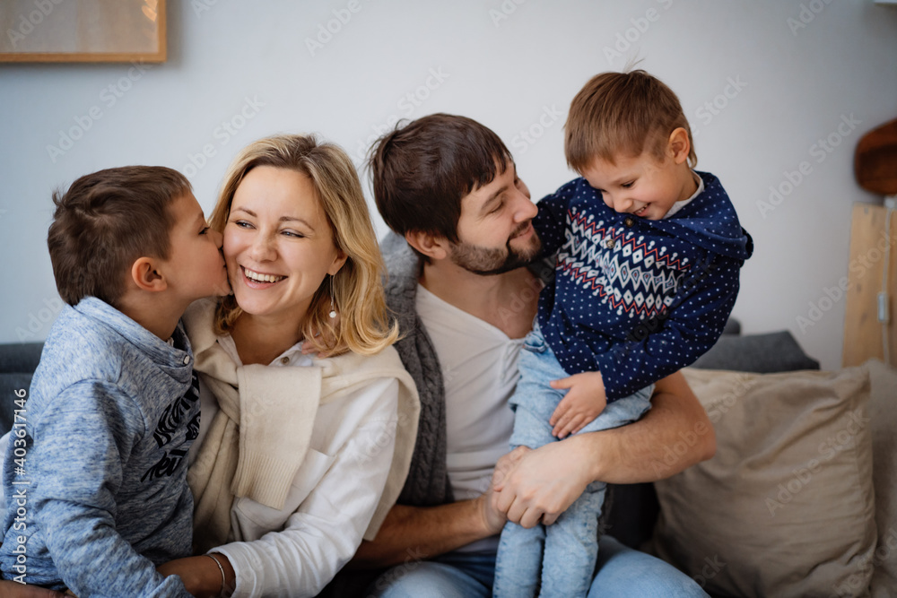 happy young loving caucasian family sitting on sofa and smiling. Son kissing his mom, dad looking with love at his little boy. Image with selective focus happy young loving caucasian family sitting on sofa and smiling. Son kissing his mom, dad looking with love at his little boy. Image with selective focus