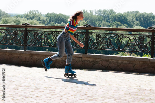Cheerful beautiful teenage girl rollerblading in the park on a warm summer morning
