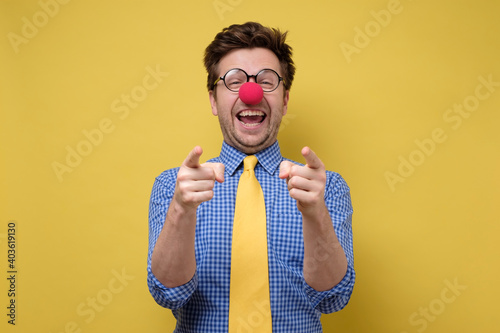 Laughing young guy dressed lika a clown pointing with finger at camera.
