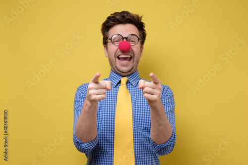 Laughing young guy dressed lika a clown pointing with finger at camera. photo