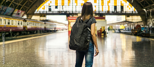 Back view of young asian woman traveler with small backpack on the railway stantion.Waiting for train for transport on holiday trip.Travel concept