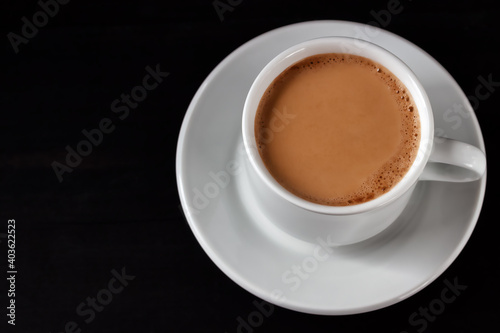 Coffee with cream in a white cup on a black wooden table