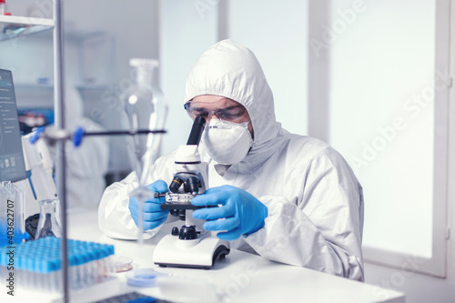 Microbiologist examining virus evolution using high tech microscope dressed in ppe suit. Virolog in coverall during coronavirus outbreak conducting healthcare scientific analysis.