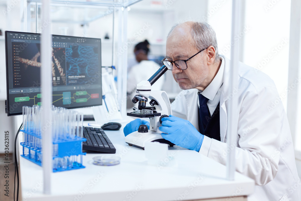 Senior scientist in chemistry laboratory uses microscope working on new medicine. Chemist researcher in sterile lab doing experiments for medical industry using modern technology.