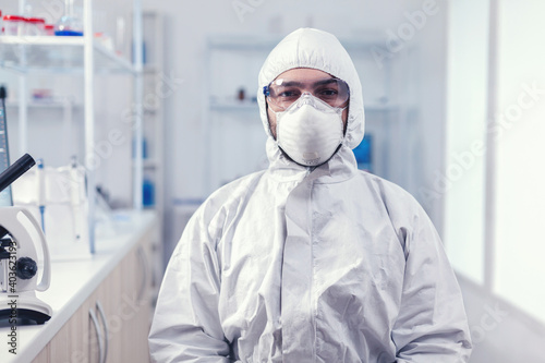Portrait of tired scientist wearing coverall with protection glasses looking at camera in medicine laboratory. Overworked researcher dressed in protective suit against invection with coronavirus photo