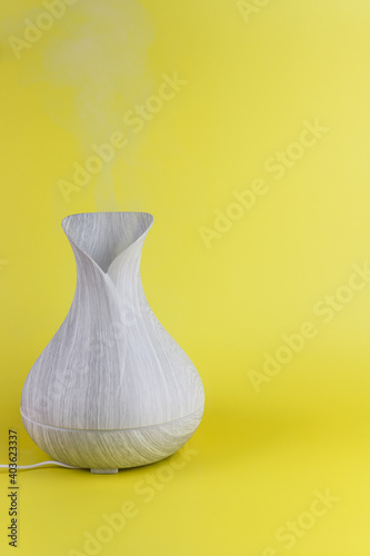 Grey aroma diffuser with steam from water and oil on yellow background
